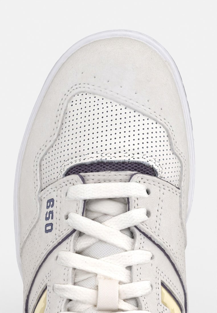 Sneaker z białą zamszową cholewą z perforowanymi sekcjami. Sznurowadła w jasnoszarym kolorze, małe niebieskie logo i biała gumowa podeszwa.
