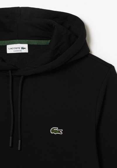 Hoodie noir en matériau doux avec une coupe classique. Il comprend une capuche avec cordon de serrage et un petit logo crocodile brodé en vert.