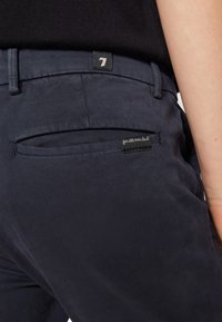 Pantaloni blu navy realizzati in morbido cotone misto, dotati di una tasca posteriore con dettagli di cucitura e un'etichetta, che mostrano un design minimalista.
