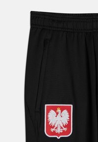 Černé tepláky s elastickým pasem, se bočními kapsami a výrazným vyšitým emblémem polského orla v bílé a červené barvě.