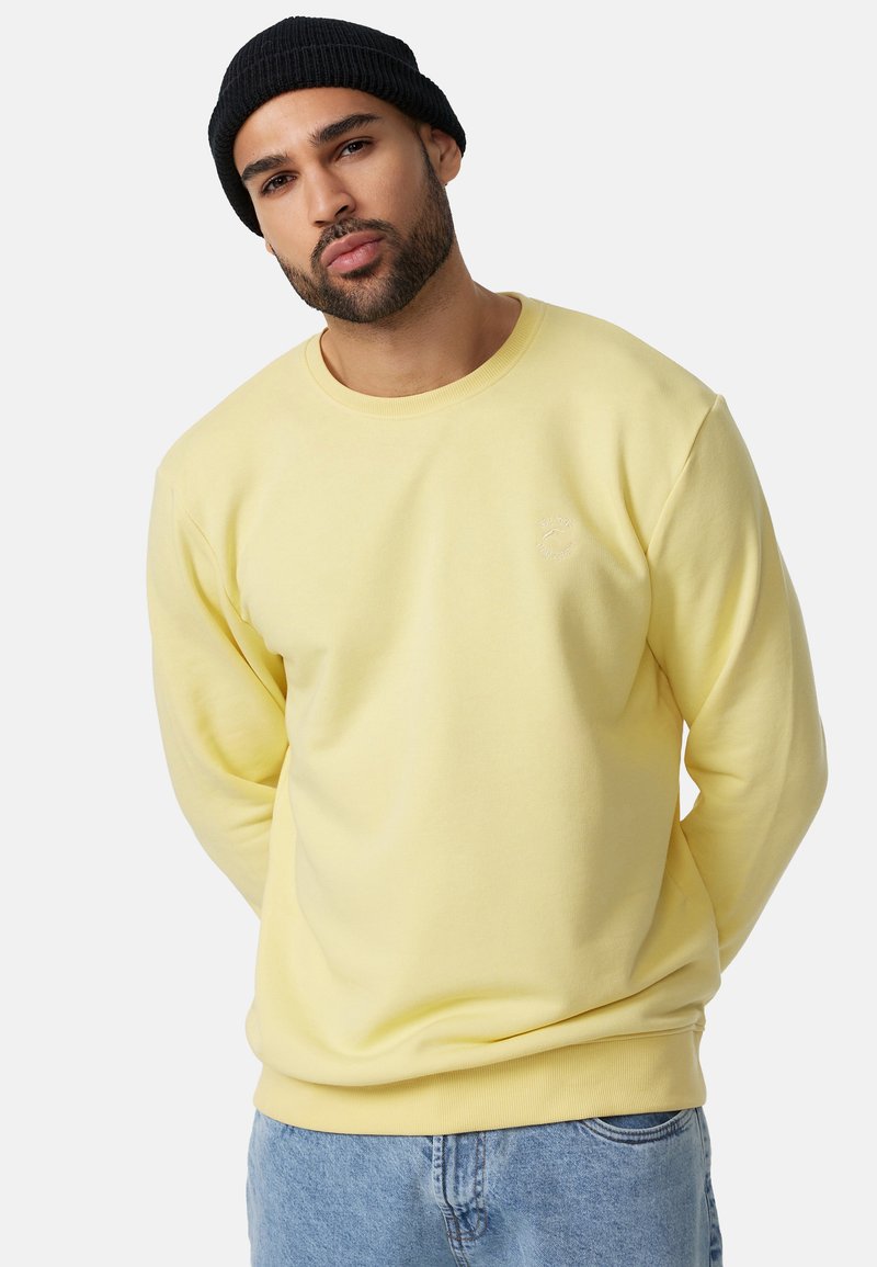 Gul crewneck sweatshirt i blødt materiale med ribstrikkede manchetter og kant; broderet logo på brystet; stylet med blå denim jeans og sort hue.