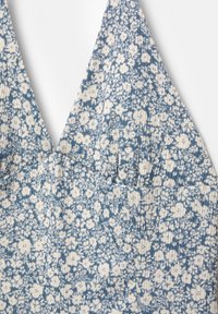 Cvetni material v modri in beli barvi, z globokim V-izrezom in rebrasto teksturo, ki poudarja oprijet bodice ter detajle z naborki.