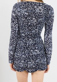 Marinblommig klänning med rynkad design, långa ärmar och scallopad fåll, tillverkad av lätt, strukturerad tyg med små blå blommor.