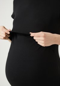 Črna obleka s prilegajočim se krojem, izdelana iz raztegljive tkanine, s kratkimi rokavi in nabrano podrobnostjo v pasu, kar poudarja raztegljiv fit.