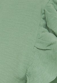 Tissu texturé vert présentant de douces plis, créant une apparence en couches. Le matériau est léger et a une sensation subtile et respirante.