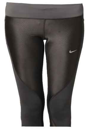 Femme portant un top de sport sans manches noir, des leggings courts noirs avec le logo Nike, et des chaussures de course noires, debout devant un fond uni.