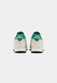 Tenisky New Balance s šedým a bílým svrškem, zelenými akcenty, semišovými panely a černou gumovou podrážkou, z pohledu zezadu.