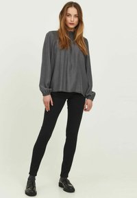 Blusa gris de manga larga con textura fruncida en el escote, combinada con jeans skinny negros y mocasines negros. Tejido suave, corte relajado.