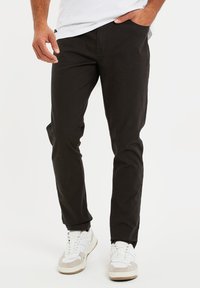 Zwarte chino's met een slim fit, gemaakt van katoen. Voorzien van zijzakken en een gladde textuur, gecombineerd met witte en grijze sneakers.