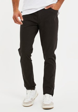 Zwarte chino's met een slim fit, gemaakt van katoen. Voorzien van zijzakken en een gladde textuur, gecombineerd met witte en grijze sneakers.