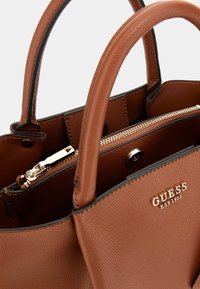 Brown leather handbag with textured exterior, zippered closure, and metallic hardware. Features short, rounded handles; logo visible.