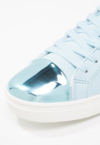 Baskets bleu clair avec semelle blanche, lacets assortis et embout métallique argenté réfléchissant.