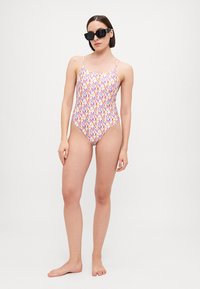 One-piece swimsuit with colorful logo pattern in pink, orange, and blue. Features thin adjustable straps and a low back design.
