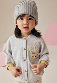 Szary kardigan na guziki z prążkowanymi mankietami i haftowanym wzorem misia, noszony z jasnoszarym prążkowanym dzianinowym beanie.