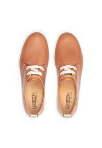 Zapatos de cuero marrón perforados con cordones blancos y una suela de goma blanca. El interior presenta una plantilla color marrón claro con detalle del logo. Forma redondeada.
