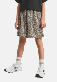 Gonna a pieghe con stampa leopardata in beige e nero, abbinata a sneaker bianche e calzini crema. Look casual, vestibilità rilassata con un design di lunghezza media.