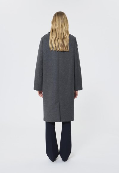 Caban gri din lână, cu mâneci lungi, croială dreaptă și detalii pe cusătura din spate, asortat cu pantaloni bleumarin. Textură moale, design minimalist.