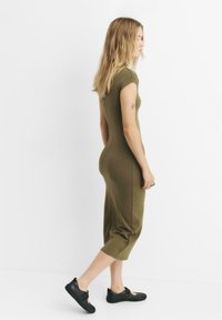 Olívová priliehavá šaty s krátkymi rukávmi, po kolená, s hladkou textúrou. Nosí sa s čiernymi balerínami s detailom remienka.