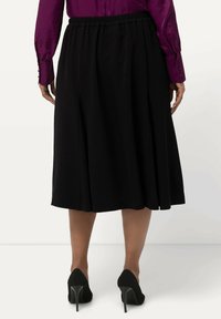 Zwarte geplooide rok met een elastische tailleband, die net onder de knie valt. Gemaakt in combinatie met zwarte gestructureerde hoge hakken en een paarse blouse.