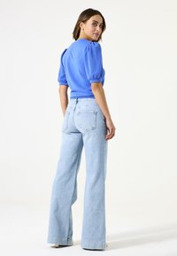 Suéter de manga abullonada en azul claro combinado con unos vaqueros de denim claro de pierna ancha de cintura alta, que muestran un ajuste relajado y una textura suave.