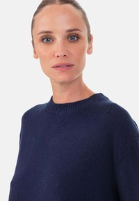 Pull en tricot bleu marine avec un col rond et des bordures côtelées. La texture est douce et le design présente une coupe décontractée avec des manches longues.