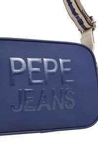 Donkerblauwe rechthoekige tas gemaakt van gestructureerd materiaal, voorzien van verhoogde "PEPE JEANS" opdruk. Inclusief een verstelbare schouderband met een patroon.