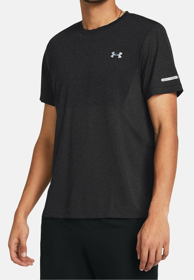 Hombre que lleva una camiseta atlética negra de manga corta con el logo de Under Armour en el pecho y una franja reflectante en la manga izquierda.