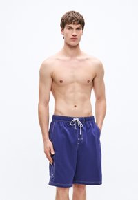 Μωβ μαγιό βερμούδα με κορδόνι στη μέση, λευκή ραφή και πλαϊνή τσέπη. Το υλικό φαίνεται ελαφρύ και λείο. Δεν φοριέται μπλούζα.