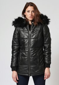 Giacca in pelle nera con design trapuntato, chiusura con zip, due tasche laterali e cappuccio in pelliccia sintetica rimovibile. I polsini a coste completano il look.