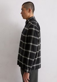 Chemise à carreaux noir et blanc à manches longues avec col boutonné, poche poitrine et tissu texturé, vue de côté.