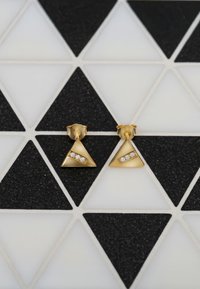 Boucles d'oreilles triangulaires en or avec une rangée diagonale de trois petites pierres claires. Surface lisse et réfléchissante avec une finition polie.