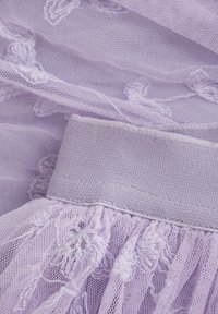 Lila spets tyg med broderade blommönster, med ett slätt, solid lila midjeband. Genomskinlig textur och volangkant synlig.