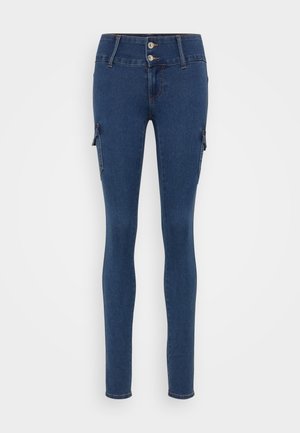 Smalje jeans laget av mørk blå denim. Har høy midje, lukking med to knapper, og sidelommer med glidelåsdetaljer. Glatt tekstur.