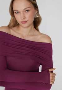 Burgunderfarbene Off-Shoulder-Bluse mit langen Ärmeln, glatter Textur und drapiertem Stoffdetail am Ausschnitt.