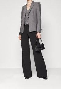 Blazer gris à carreaux porté sur un gilet gris, associé à un pantalon large noir et un petit sac à main noir avec des accents de ferrures argentées.
