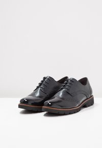  Scarpe oxford in vernice nera con dettagli a brogue, punta tonda e design con lacci, dotate di suola in gomma con accenti testurizzati.