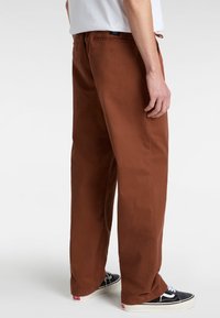 Pantalons marron à jambes larges en coton, dotés de poches arrière et d'une texture lisse. Associés à des baskets noires.