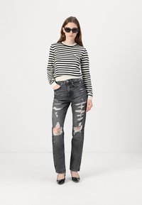 Sorte og hvite stripete langermede skjorte kombinert med lys grå slitte jeans. Jeansene har flere revne områder, og svarte slipsåler.