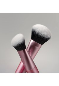 Deux pinceaux de maquillage croisés avec des poils doux, denses, noirs et blancs et des manches métalliques roses étiquetés RT459 sur un fond neutre.