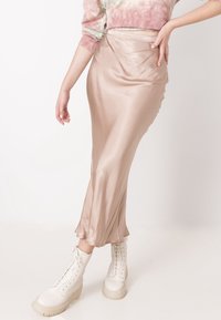 Gonna midi in satin beige morbido con vita aderente e orlo svasato. Abbinata a stivali bianchi con lacci e suole spesse.