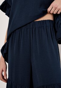 Navy blue, textured fabric outfit featuring a loose top with ruffled sleeves and gathered waist pants; layered design with a relaxed fit.