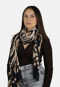 Sciarpa animalier in tonalità di nero, beige e rosa chiaro; tessuto morbido con drappeggio fluido; indossata su una camicetta scura aderente.