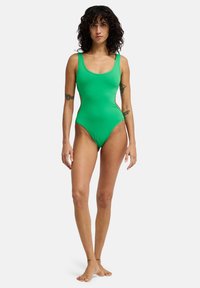 Πράσινο ολόσωμο μαγιό με λαιμόκοψη scoop, μεσαίου πλάτους τιράντες και ψηλή κοπή στα πόδια. Λείο υλικό, μίνιμαλ σχεδιασμός και εφαρμοστή γραμμή.