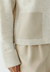 Strickpullover in hellbeige mit gerippten Bündchen, ausgestattet mit einem glatten, beigen Lederpatch auf der Vorderseite und einer lockeren Silhouette.