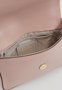 Interiér růžové kožené tašky DKNY, s hladkou texturou, zlatými kovovými prvky, kapsou na karty a podšitým oddílem.