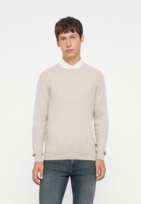 Lys beige genser med ribbet tekstur, rund halsutringning og lange ermer, sammen med mørk denimjeans. Enkel og uformell design.
