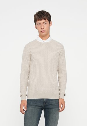 Lys beige genser med ribbet tekstur, rund halsutringning og lange ermer, sammen med mørk denimjeans. Enkel og uformell design.
