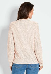 Hellrosa gestrickter Pullover mit Rippstrickstruktur und langen Ärmeln. Verfügt über einen runden Ausschnitt und elastische Bündchen. Kombiniert mit blauen Jeans.