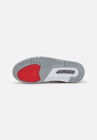 Suela de zapatilla de goma gris con acentos rojos y un patrón circular. Presenta líneas de agarre texturizadas y la marca “JORDAN” en la superficie blanca.