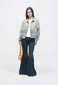 Gaiši mazgāta džinsa jaka ar izbalējušām piedurknēm, balta T-krekls, tumši uzplaļņotas džinsas un oranža plecu soma ar spīdīgu apdari.